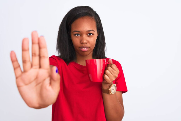Mladý africký Američan žena pití šálek kávy na izolovaném pozadí s otevřenou rukou dělat stop znamení s vážným a sebejistý výraz, obrana gesto - Fotografie, Obrázek
