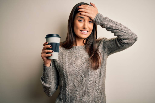 Young beautiful brunette woman drinking glass of coffee over isolated white background stressed with hand on head, shocked with shame and surprise face, angry and frustrated. Fear and upset for mistake. - Fotografie, Obrázek