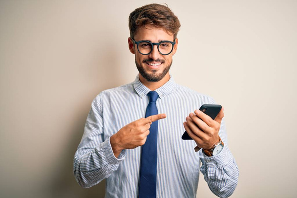 Jeune homme d'affaires ayant une conversation à l'aide d'un smartphone sur fond blanc très heureux pointant avec la main et le doigt
 - Photo, image