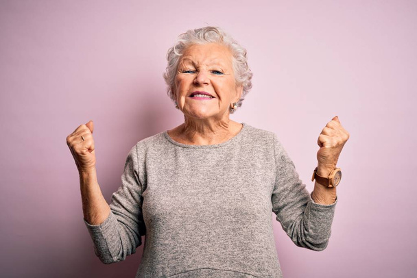 Starsza piękna kobieta w luźnej koszulce stojąca na odizolowanym różowym tle bardzo szczęśliwa i podekscytowana wykonując gest zwycięzcy z podniesionymi ramionami, uśmiechnięta i krzycząca o sukces. Koncepcja uroczystości. - Zdjęcie, obraz