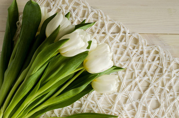 White tulips lying on a white wicker napkin and a light wooden table. - Foto, imagen