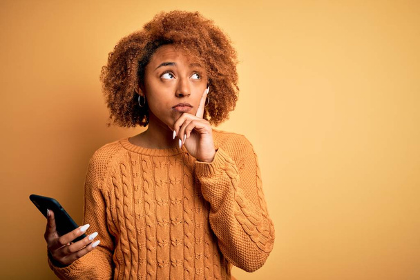 Jovem afro americano Africano mulher com cabelo encaracolado ter conversa usando smartphone rosto sério pensando em questão, ideia muito confusa
 - Foto, Imagem