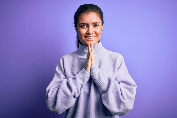 Young beautiful woman with blue eyes wearing casual turtleneck sweater over pink background praying with hands together asking for forgiveness smiling confident. - Photo, Image