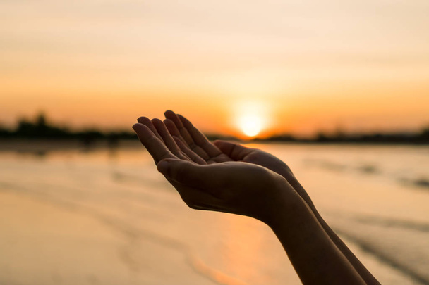 Γυναίκα χέρια τόπο μαζί, όπως προσεύχεται μπροστά από τη φύση θόλωμα παραλία ηλιοβασίλεμα ουρανό φόντο. - Φωτογραφία, εικόνα