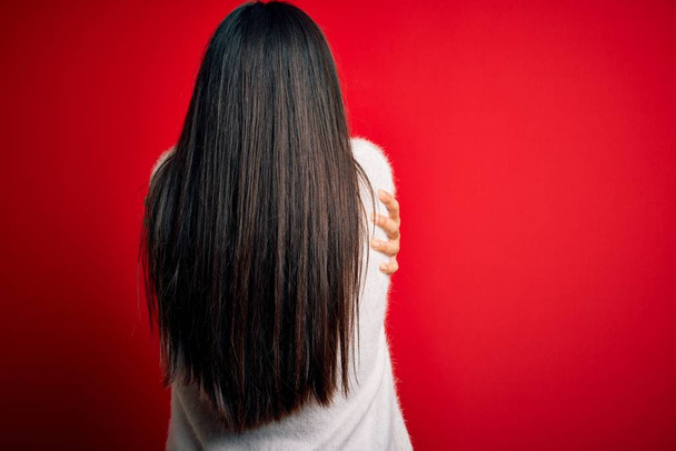 Young beautiful asian woman wearing casual sweater and glasses over red background Hugging oneself happy and positive from backwards. Self love and self care - Photo, Image