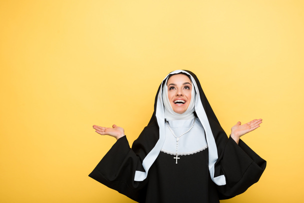 cheerful nun praying and looking up, on yellow - 写真・画像