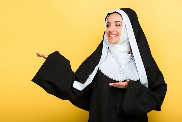 beautiful cheerful nun presenting something, on yellow - Fotografie, Obrázek