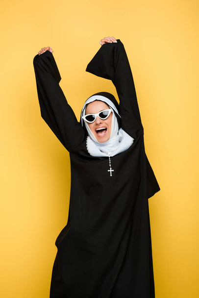 attractive excited nun dancing in sunglasses isolated on yellow - Φωτογραφία, εικόνα