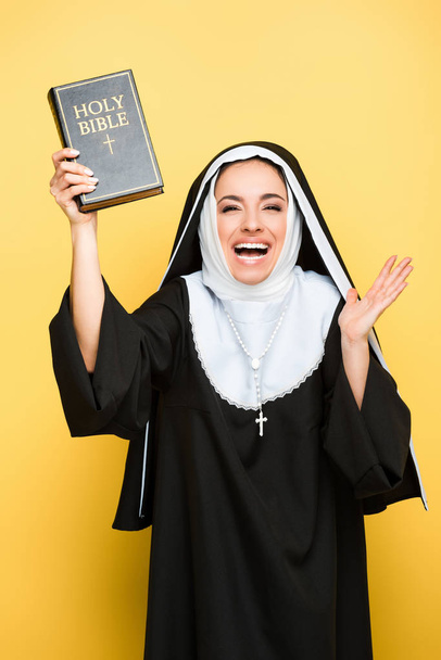 krásná vzrušená jeptiška držící svatou Bibli na šedé - Fotografie, Obrázek
