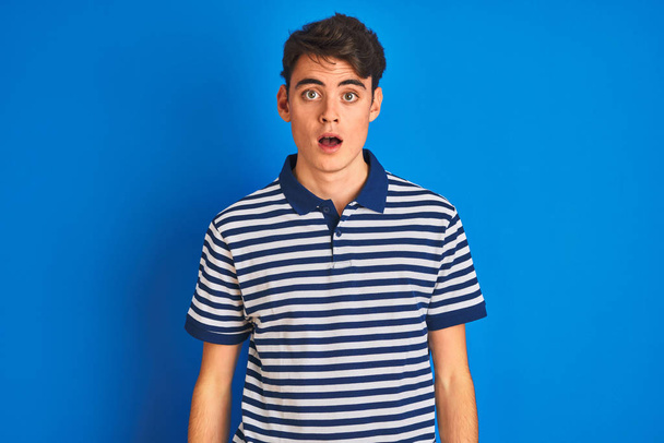 Adolescente niño vistiendo casual camiseta de pie sobre azul aislado fondo miedo y conmocionado con sorpresa y expresión asombrada, miedo y cara emocionada
. - Foto, Imagen