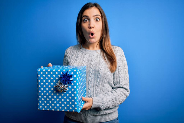 Jeune femme blonde tenant une boîte cadeau comme cadeau d'anniversaire sur fond isolé effrayé en état de choc avec un visage surprise, effrayé et excité par l'expression de la peur
 - Photo, image