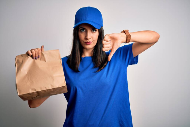 Giovane donna di consegna con gli occhi azzurri che indossa cappuccio che tiene sacchetto di carta con cibo con faccia arrabbiata, segno negativo che mostra antipatia con i pollici verso il basso, concetto di rifiuto
 - Foto, immagini