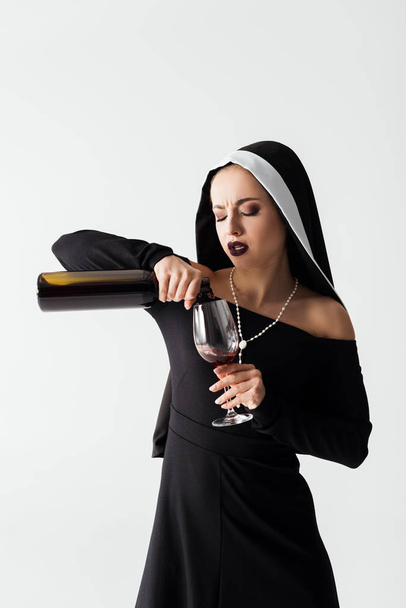 attractive sexy nun pouring wine from bottle into glass isolated on grey - 写真・画像