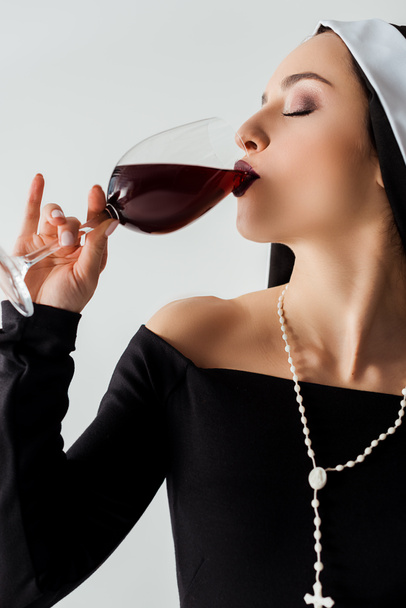 ελκυστική αισθησιακή καλόγρια πίνοντας κόκκινο κρασί από γυαλί απομονωμένο σε γκρι - Φωτογραφία, εικόνα