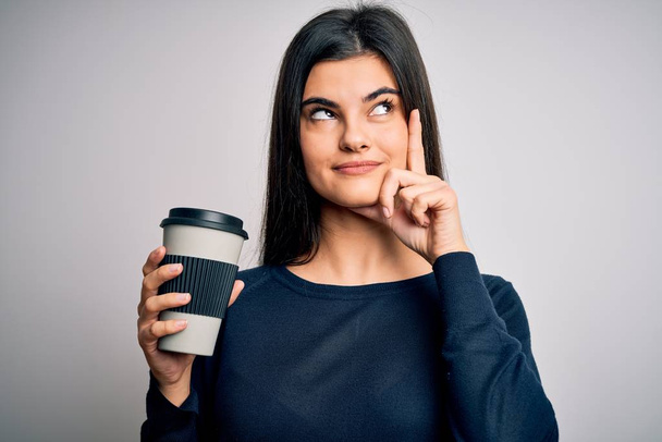 Młoda piękna brunetka pije filiżankę kawy na odizolowanym białym tle poważna twarz myśląc o pytaniu, bardzo zdezorientowany pomysł - Zdjęcie, obraz