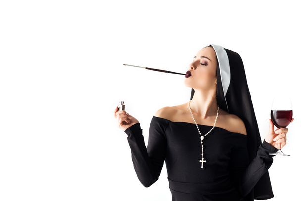 attractive sexy nun with lighter and glass of wine smoking a cigarette in mouthpiece isolated on white - Photo, Image