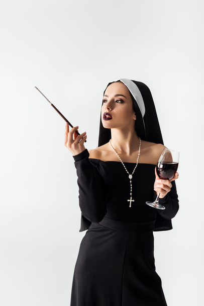 attractive nun with glass of wine smoking a cigarette in mouthpiece isolated on grey  - Фото, зображення