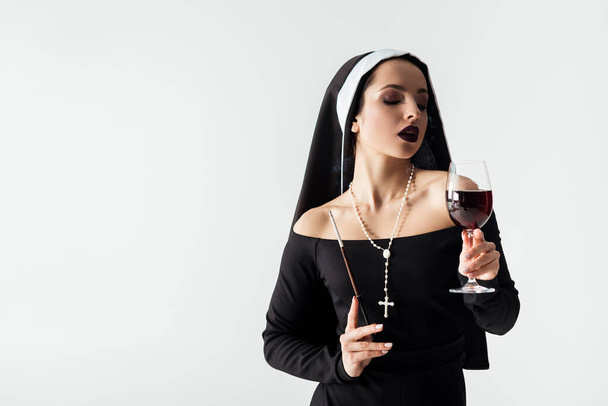 beautiful sensual nun holding glass of wine and cigarette in mouthpiece isolated on grey  - Fotoğraf, Görsel