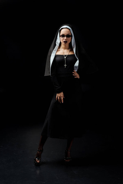 beautiful sexy nun in black dress and sunglasses, on black   - Fotó, kép