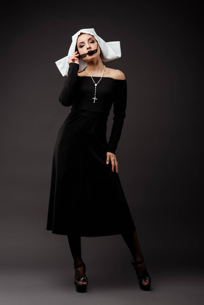 sexy nun in black dress and sunglasses, on grey - Foto, afbeelding