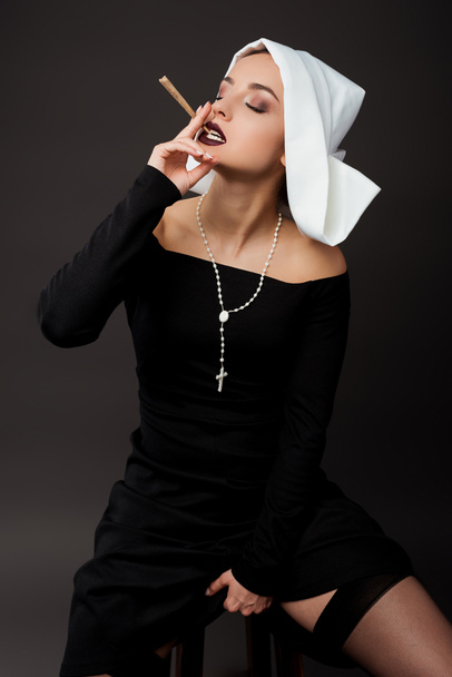 attractive sexy nun smoking marijuana joint on grey - Photo, Image