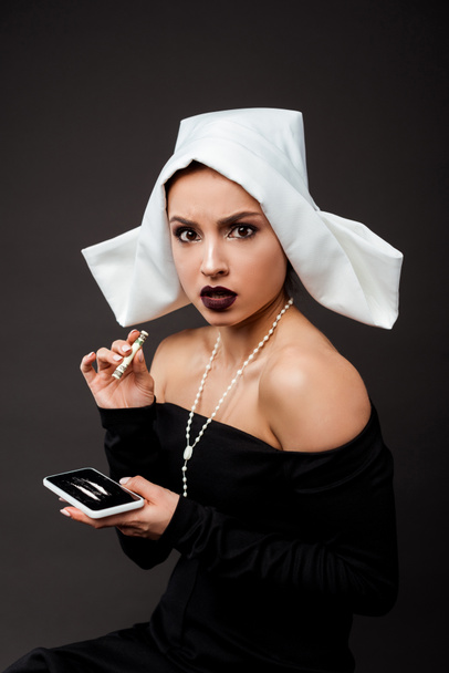 emotional sexy nun holding dollar banknote and smartphone with cocaine lines on grey - Photo, Image