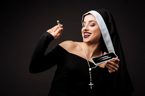 счастливая монахиня держит доллар банкноты и смартфон с кокаином линии изолированы на серый
 - Фото, изображение