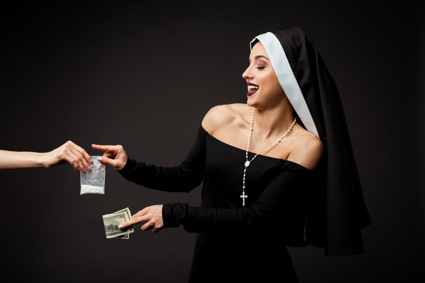 smiling sexy nun with money buying plastic bag of cocaine isolated on grey - Photo, Image