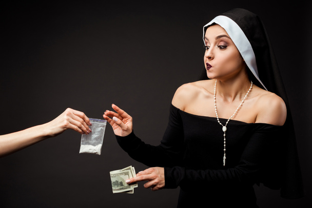 Nachdenkliche Nonne mit Geld kauft Plastiktüte mit Kokain isoliert auf grau - Foto, Bild