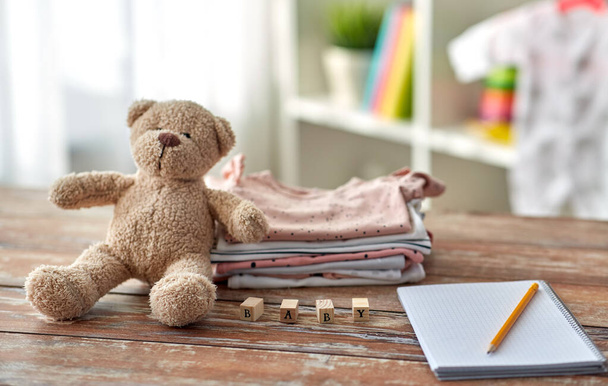baby clothes, teddy bear, toy blocks and notebook - Zdjęcie, obraz