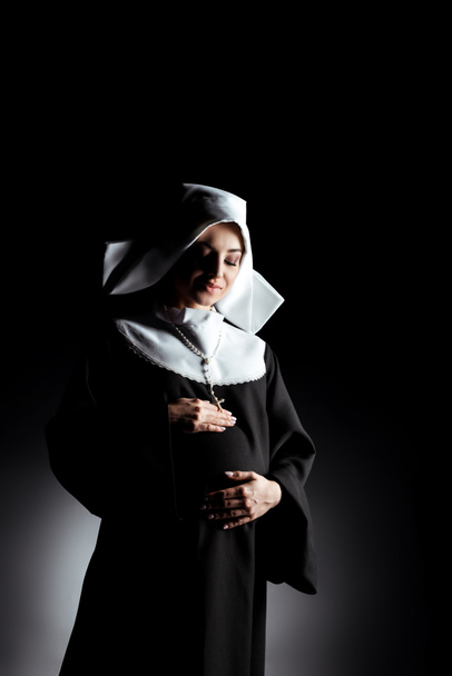 όμορφη ευτυχισμένη έγκυος καλόγρια αγγίζοντας την κοιλιά σε μαύρο - Φωτογραφία, εικόνα
