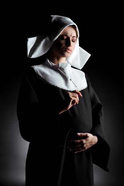 worried pregnant nun holding cross and touching belly on grey - Photo, Image