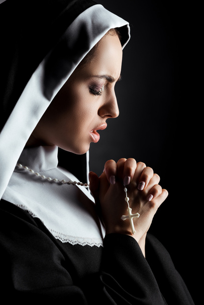 beautiful worried nun praying with cross isolated on black - Photo, Image