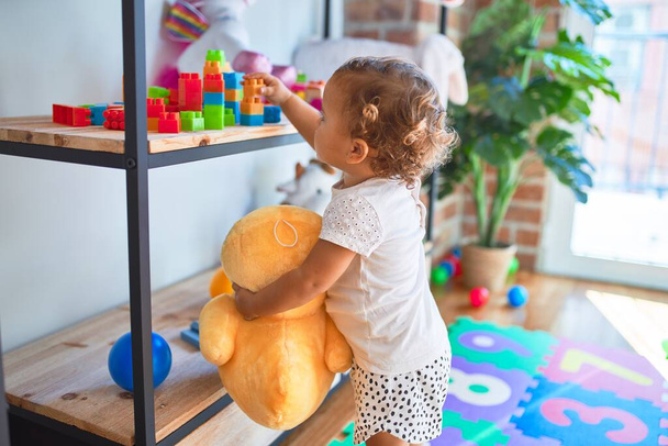 Roztomilé batole drží kachní panenku stojící kolem spousty hraček ve školce - Fotografie, Obrázek