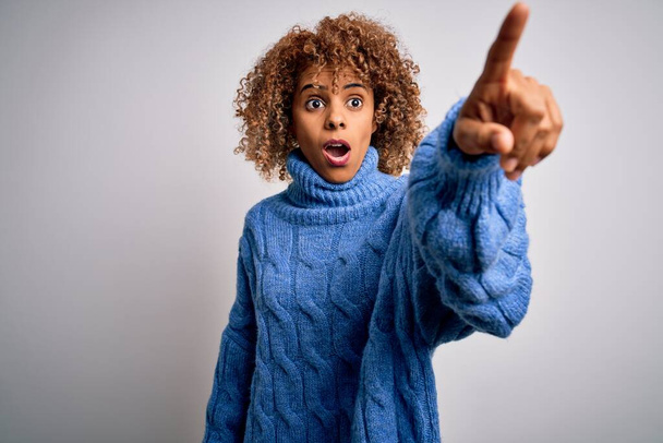 Junge schöne afrikanisch-amerikanische Frau trägt Rollkragenpullover über weißem Hintergrund Zeigt mit dem Finger überrascht voraus, offener Mund erstaunten Ausdruck, etwas auf der Vorderseite - Foto, Bild