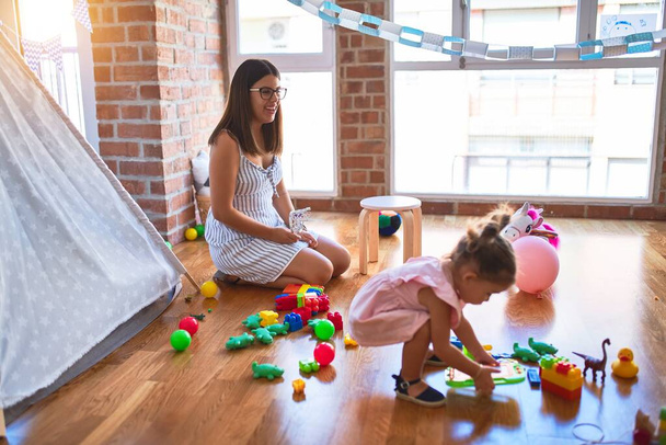 Young beautiful teacher and toddler playing at kindergarten - 写真・画像