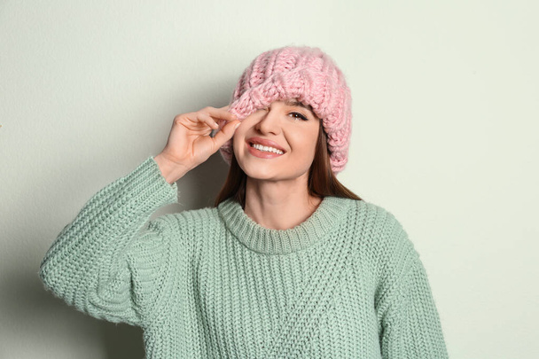 Young woman wearing warm sweater and hat on light background. Winter season - Fotó, kép