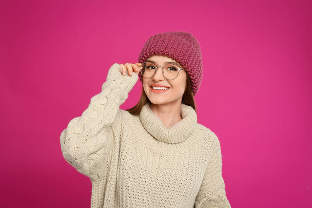 Young woman wearing warm sweater and hat on crimson background. Winter season - Fotografie, Obrázek