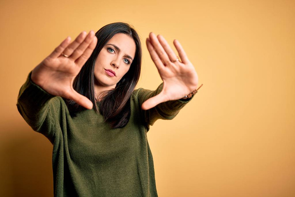 Young brunette woman with blue eyes wearing green casual sweater over yellow background doing frame using hands palms and fingers, camera perspective - Fotoğraf, Görsel