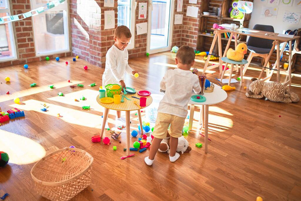 Adorable blonde twins playing around lots of toys. Cooking plastic food toy at kindergarten - 写真・画像
