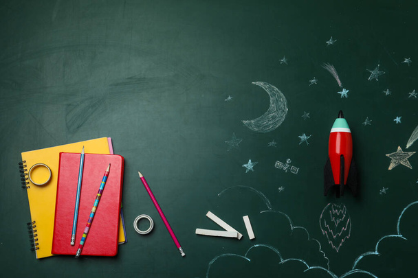 Parlak oyuncak roketi, okul malzemeleri ve karatahtadaki çizimler, düz konum. Metin için boşluk - Fotoğraf, Görsel