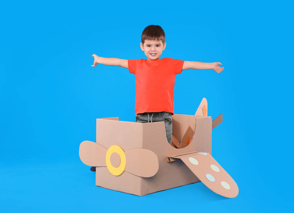 Cute little child playing with cardboard airplane on light blue background - Photo, Image
