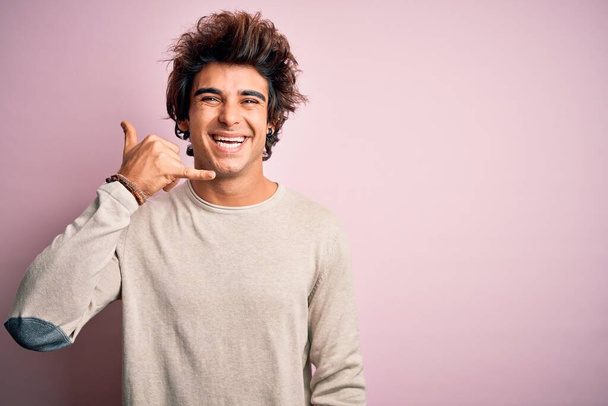 Young handsome man wearing casual t-shirt standing over isolated pink background smiling doing phone gesture with hand and fingers like talking on the telephone. Communicating concepts. - Foto, afbeelding