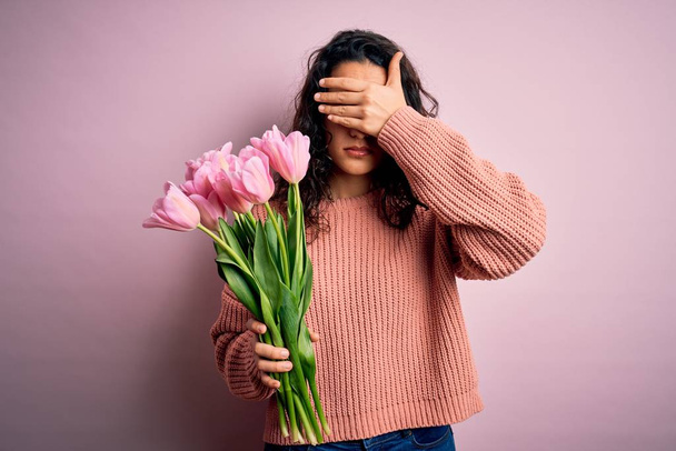 Jeune belle femme romantique avec des cheveux bouclés tenant bouquet de tulipes roses couvrant les yeux avec la main, l'air grave et triste. Concept d'appréhension, de dissimulation et de rejet
 - Photo, image