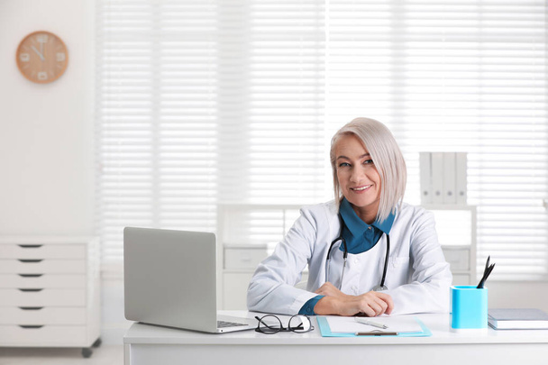 Portrait of mature female doctor in white coat at workplace - Foto, afbeelding