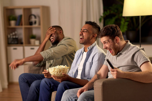 macho amigos con palomitas de maíz viendo tv en casa
 - Foto, Imagen