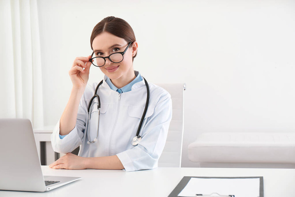 Portrait of young female doctor in white coat at workplace - Foto, Bild