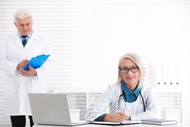Portrait of mature female doctor in white coat at workplace - Foto, Imagen