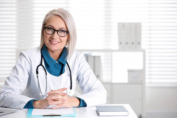 Portrait of mature female doctor in white coat at workplace - Foto, Bild