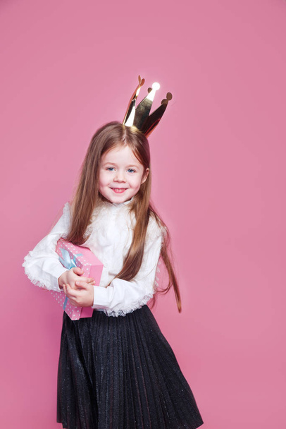 Happy little girl in crown holding birthday present box on pink background - Photo, image